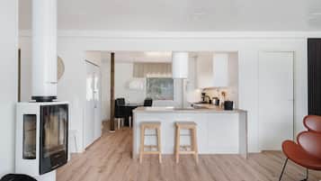 A modern kitchen with a central island, two stools, a dining area with a table and chairs, and a TV mounted on a cabinet.