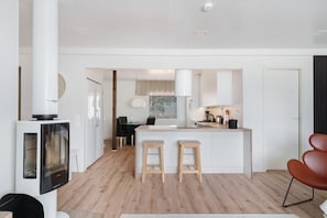 A modern kitchen with a central island, two stools, a dining area with a table and chairs, and a TV mounted on a cabinet.
