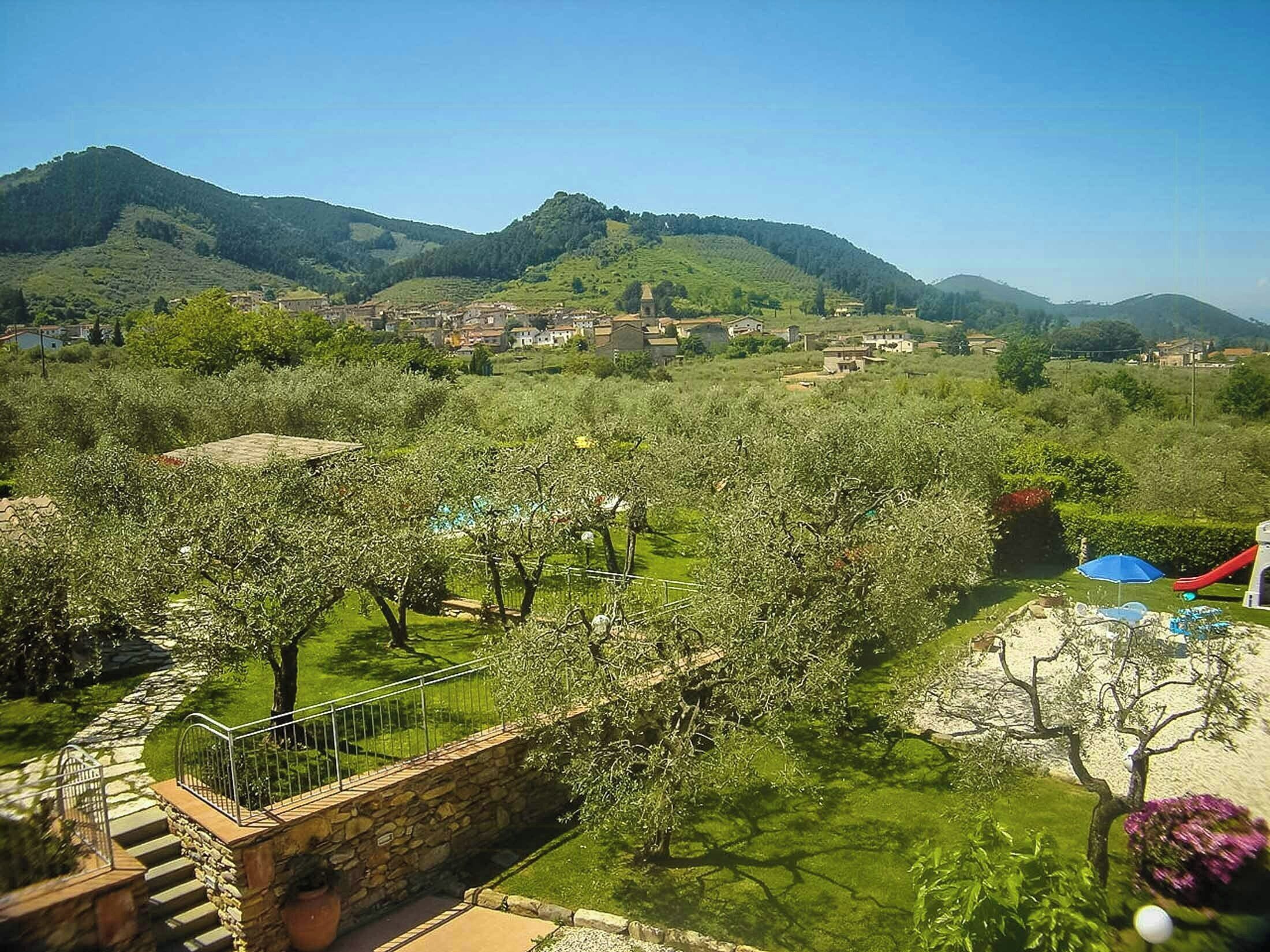Vista de maig a una vessant amb una escala de pedra que baixa, envoltada de vegetació abundant i edificis a la distància.
