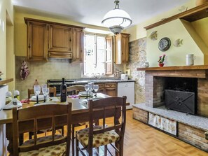 A kitchen with wooden cabinets, a dining table with chairs, a built-in oven, and a stone wall. - Apartment with pool and private terrace in Tuscany (Colle di Compito)