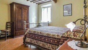 Ein Schlafzimmer mit einem hölzernen Bett, einem Nachttisch, einer Schreibtischlampe, einem Holzschrank, einem Stuhl und einem Fenster.