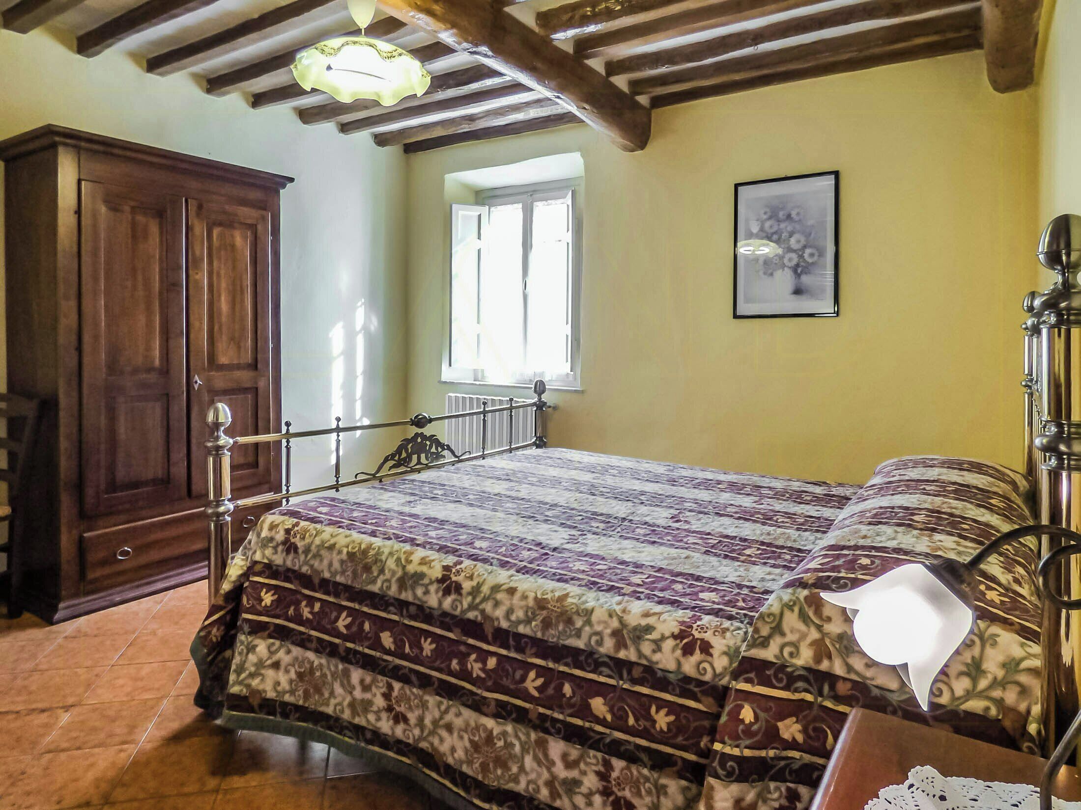 A bedroom with a bed, wooden wardrobe, window, and a lamp.