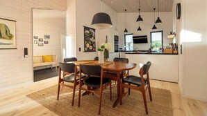 Un comedor moderno con una mesa y sillas de madera, luces colgantes y una cocina al fondo.