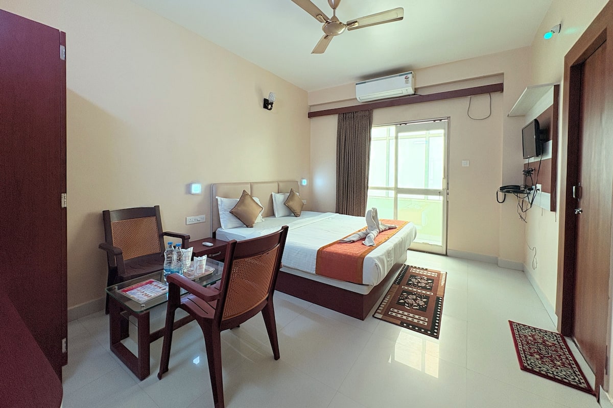 Habitación de hotel con cama, escritorio con silla, ventilador de techo, aire acondicionado, televisor y ventana con cortinas.
