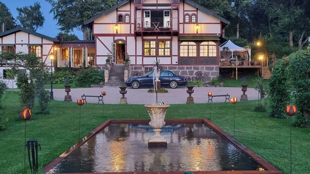 Un'ampia casa a due piani con un cortile centrale, una fontana e un'auto parcheggiata davanti.