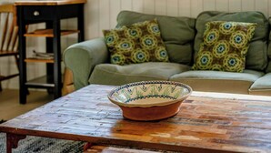 Una habitació amb un sofà verd, coixins estampats, una taula de fusta i un bol decoratiu.