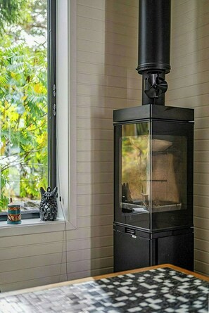 A room with a wood-burning stove, a window with a view of greenery, and a small cat figurine on the windowsill.