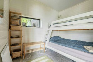 A compact room with bunk beds, a wooden shelf unit, and a window.