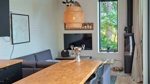 A modern living room with a wooden dining table, grey sofa, and a television. - Cottage with lake view and boat at Lake Storsjön (Sandviken)