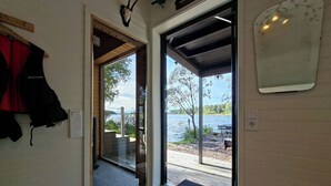 A modern interior with a glass door leading to an outdoor deck with a view of a lake. - Cottage with lake view and boat at Lake Storsjön (Sandviken)