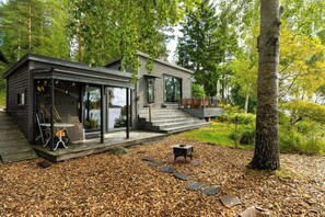 A modern cabin with a glass-enclosed porch, a deck, and a stone pathway leading to the entrance. - Cottage with lake view and boat at Lake Storsjön (Sandviken)