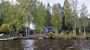 A modern house by a lake with a dock, surrounded by tall trees. - Cottage with lake view and boat at Lake Storsjön (Sandviken)
