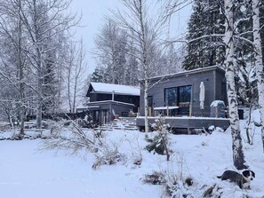 Una cabaña moderna con un balcón, rodeada de árboles cubiertos de nieve.