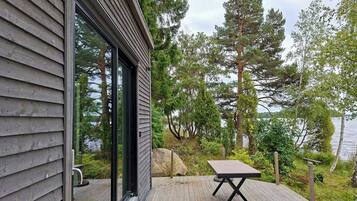 A wooden deck with a table and chairs, overlooking a lake with trees.
