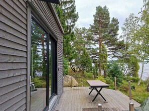 Puisesta laudasta rakennettu terassi, jossa on pöytä ja tuoleja, ja josta avautuu näkymä puita reunustamalle järvelle.