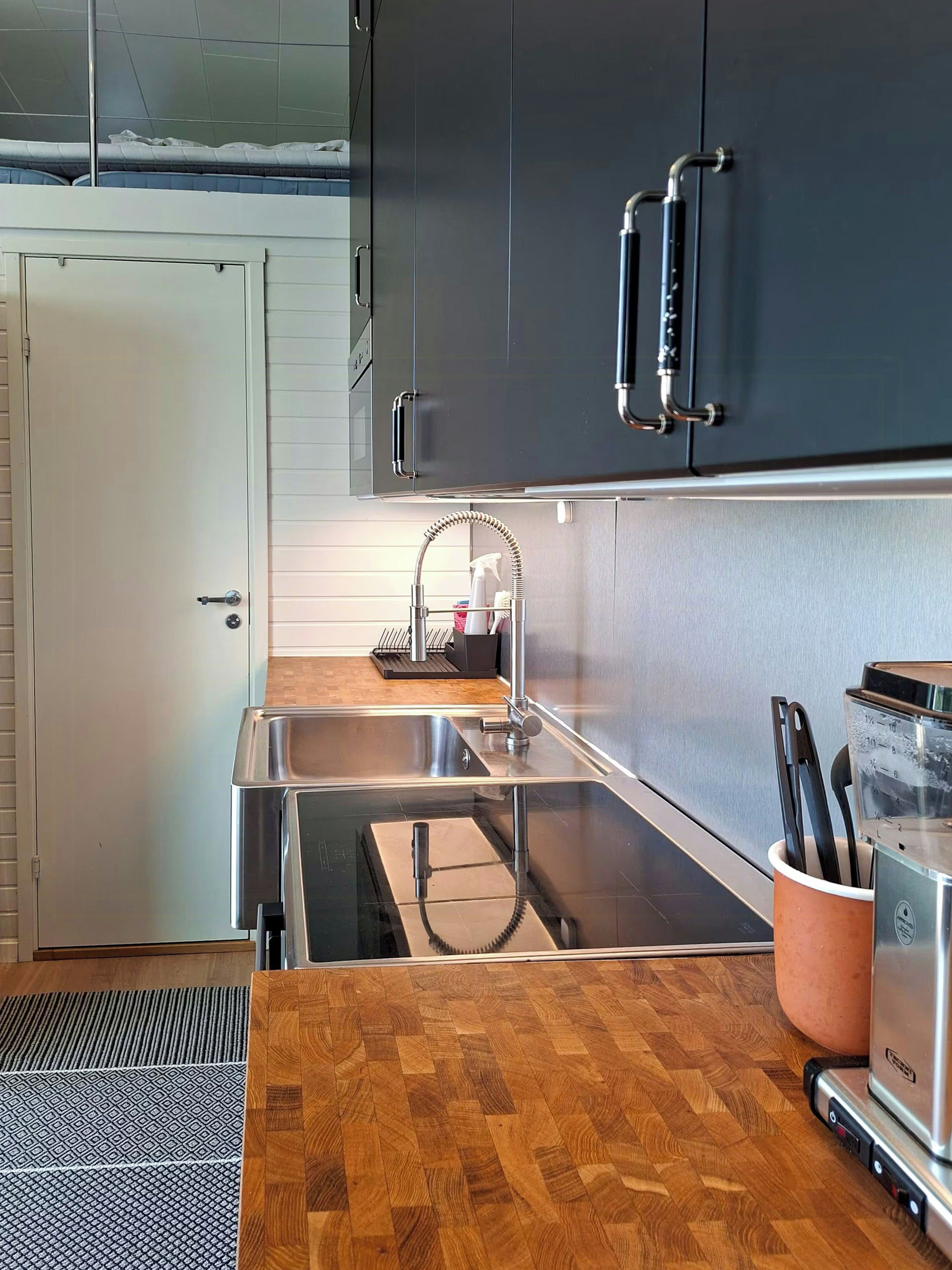 A modern kitchen with a stainless steel sink, dark cabinets, and a wooden countertop.