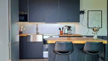 A modern kitchen with dark cabinets, a stainless steel refrigerator, a coffee machine, and two bar stools.