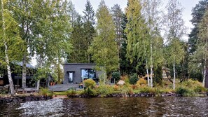 Mökki järven rannalla, jota ympäröivät puut.