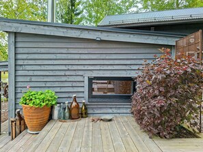 A wooden cabin with a window, a large planter with green foliage, and a metal fence.