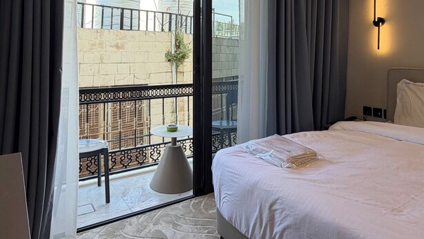 A hotel room with a bed, a balcony with a table and chairs, and a view of water tanks outside. - 201 tara-JRE Jabal Al Lweibdeh with stunning view (Amman)