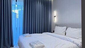 A modern hotel room with a large bed, a wall-mounted light, and a view of the outdoors through sheer curtains. - 201 tara-JRE Jabal Al Lweibdeh with stunning view (Amman)
