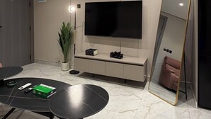 A modern living room with a flat-screen TV, a black coffee table, a sofa, a large mirror, and recessed ceiling lighting. - 201 tara-JRE Jabal Al Lweibdeh with stunning view (Amman)