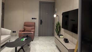 A modern living room with a sofa, a pink chair, a coffee table, a TV, and recessed ceiling lighting. - 201 tara-JRE Jabal Al Lweibdeh with stunning view (Amman)