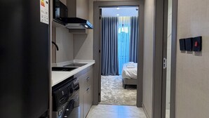 A narrow hallway with a kitchen area on the left, a bed visible through a doorway, and a bathroom on the right. - 201 tara-JRE Jabal Al Lweibdeh with stunning view (Amman)