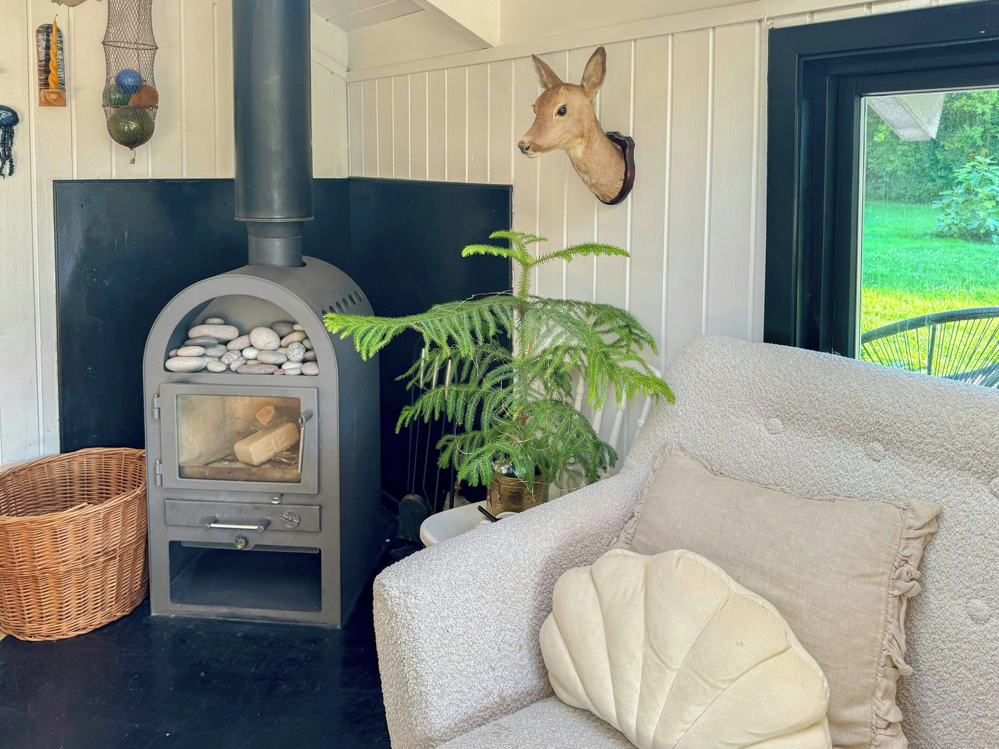 Une pièce chaleureuse avec une cheminée, un canapé, une plante de fougère et une décoration représentant une tête de cerf.