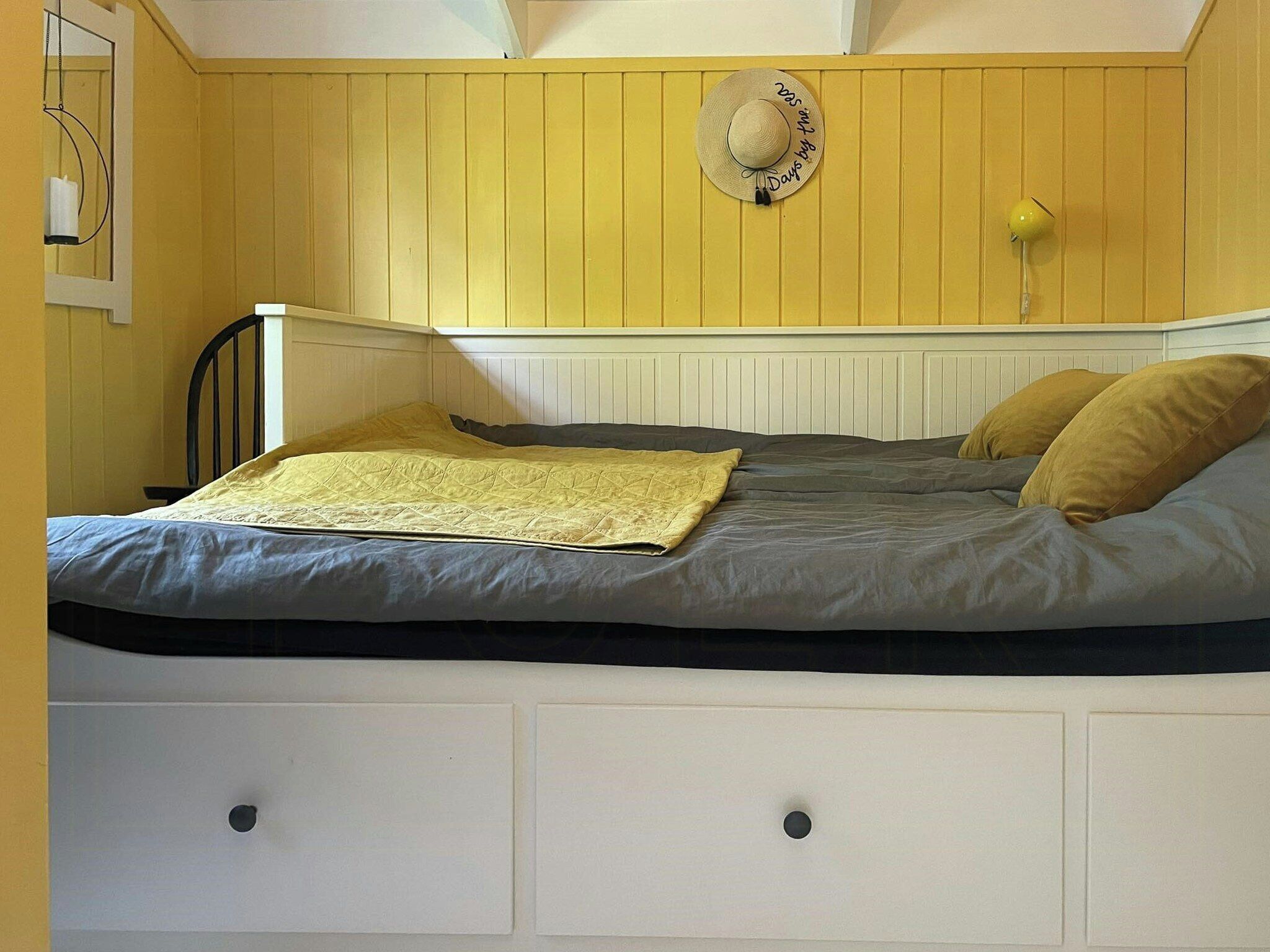A bed with a quilt, pillows, and a hat on the wall.
