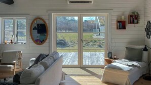 Une pièce avec un plancher en bois, des murs blancs, un canapé, un lit, un bureau et une grande fenêtre donnant sur l’extérieur.