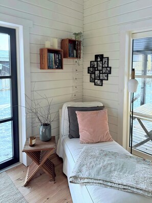 Um quarto aconchegante com cama, mesa de cabeceira e prateleira na parede com livros e objetos decorativos.