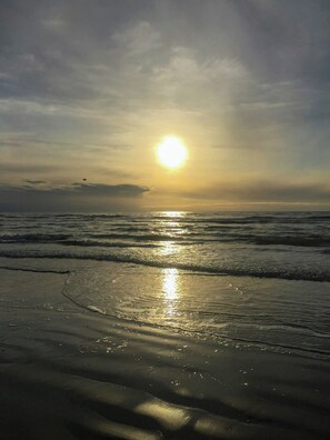 Uma praia com ondas e o sol se pondo.