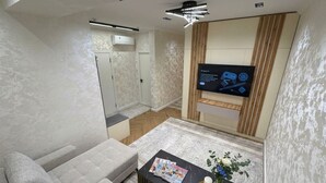 A modern living room with a sofa, a coffee table with magazines, a TV mounted on the wall, and a wooden cabinet. - Modern Apartment in Alfraganus  Rent Car & Moto (Tashkent)