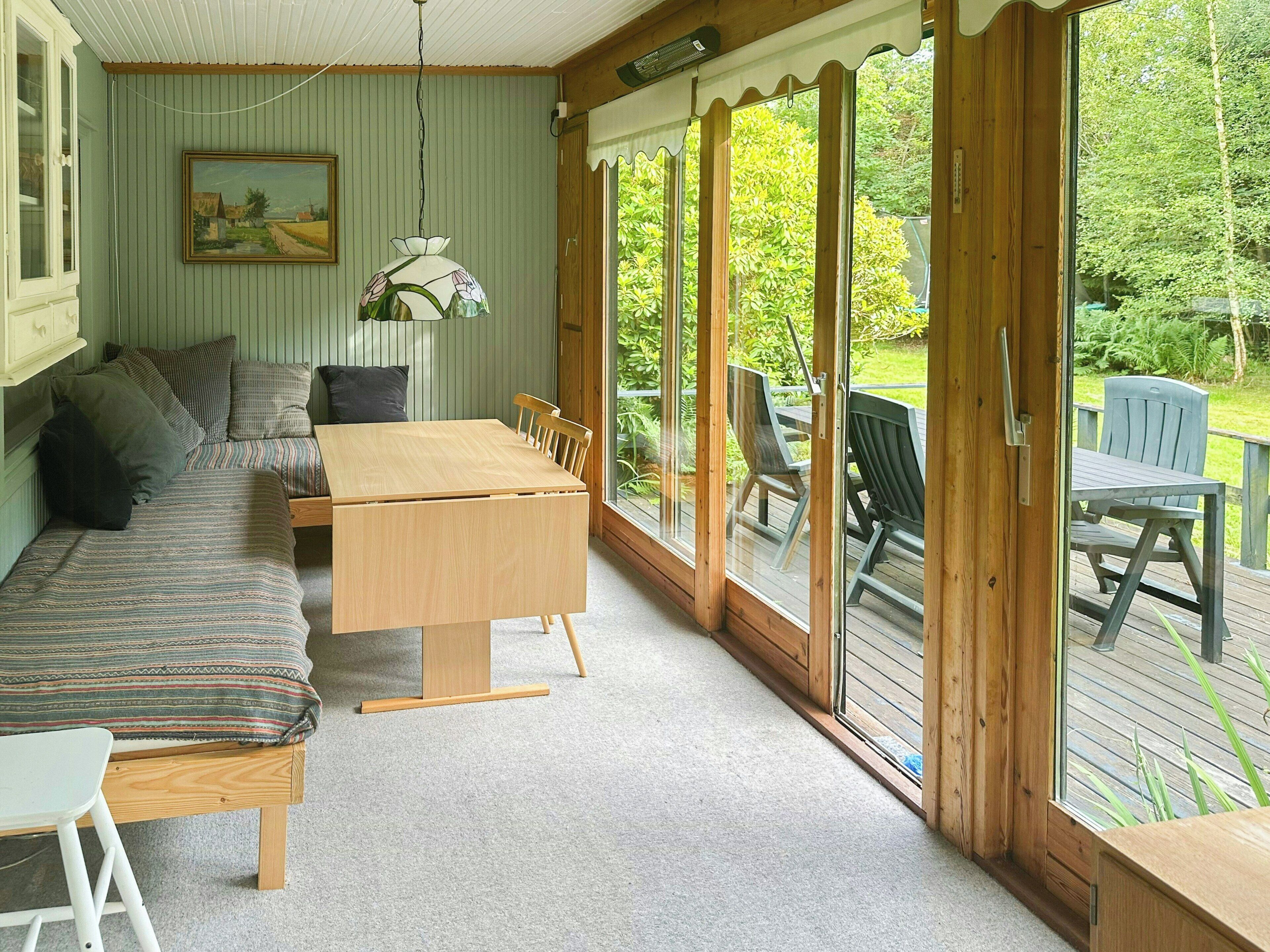 A cozy room with a wooden table, a sofa, and a large window with a view of greenery.