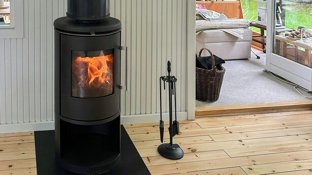 Ein modernes Interieur mit Kaminofen, Wanduhr und Blick ins Freie durch eine Glastür.