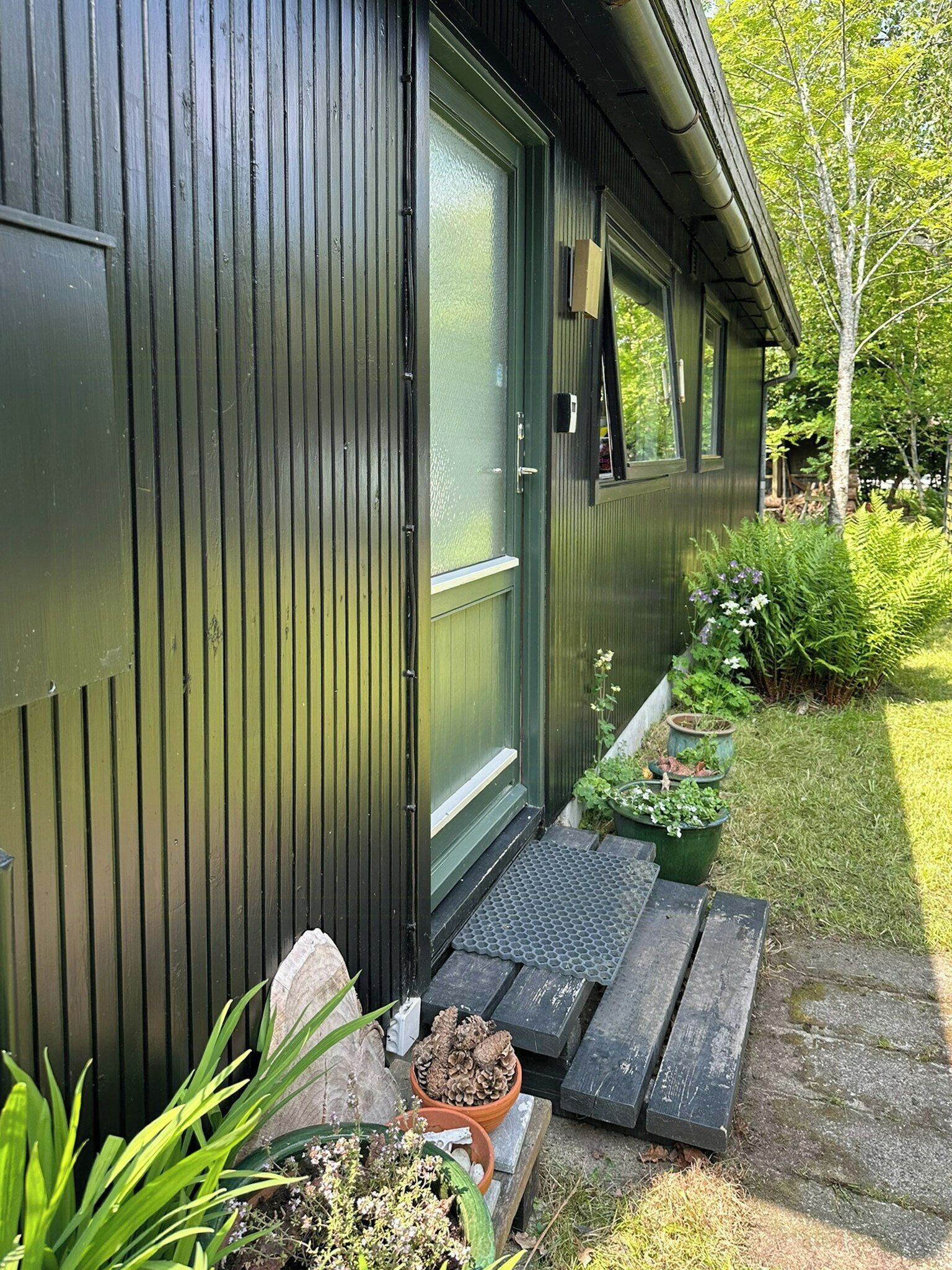 A green metal building with a door, potted plants, and a wooden bench.
