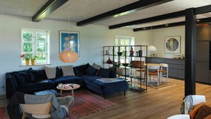 A modern living room with a dark blue sofa, a round coffee table, and a patterned rug. There is a kitchen area with a dining table and chairs visible through an open doorway. - Renovated farmhouse with starry sky views (Barrit)