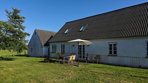 Una casa amb un terrat inclinat, un pati amb mobles d'exterior i un parasol gran.