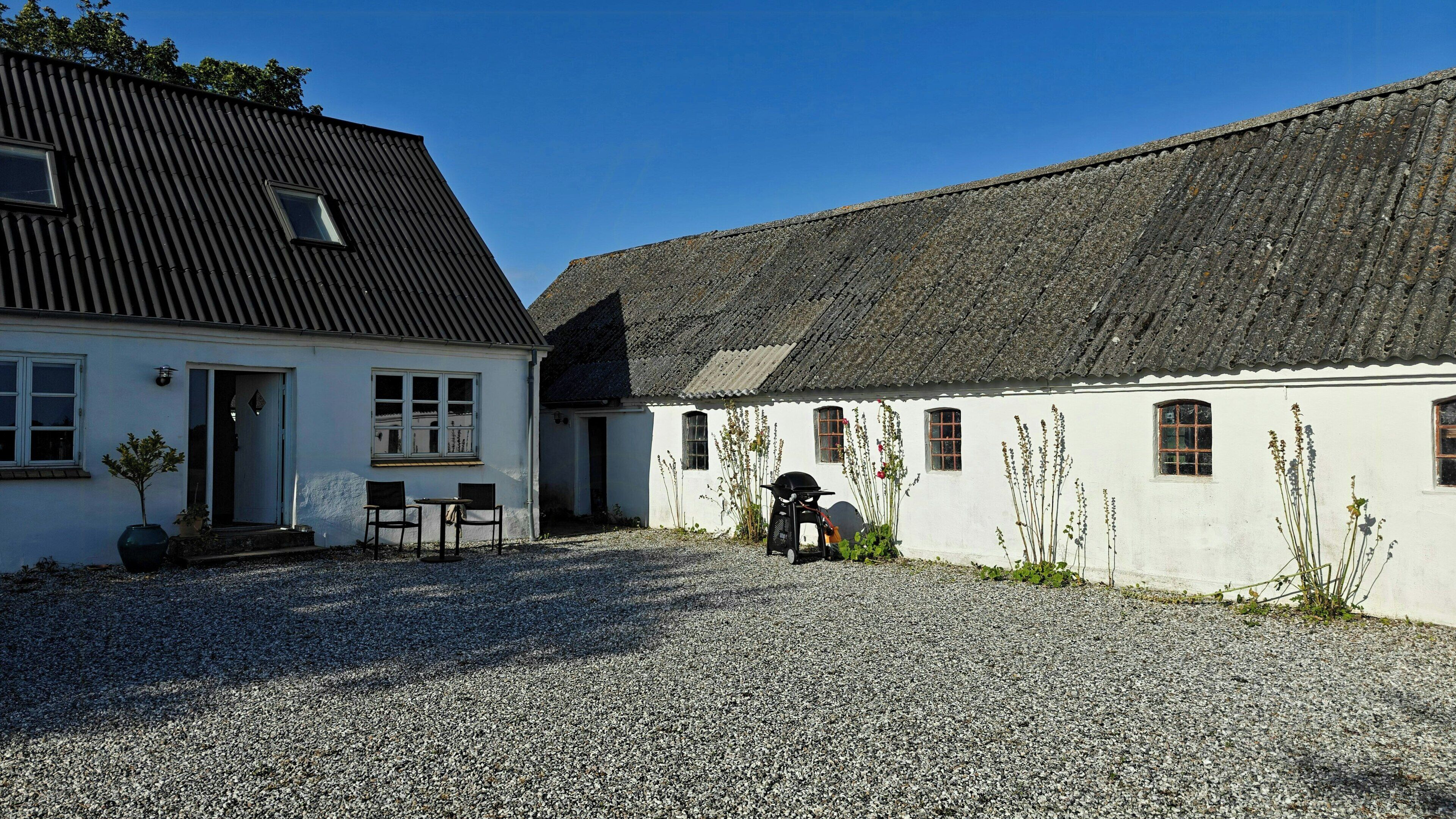 Une cour recouverte de gravier, avec un bâtiment blanc doté d’un toit noir et d’un toit traditionnel en tuiles.