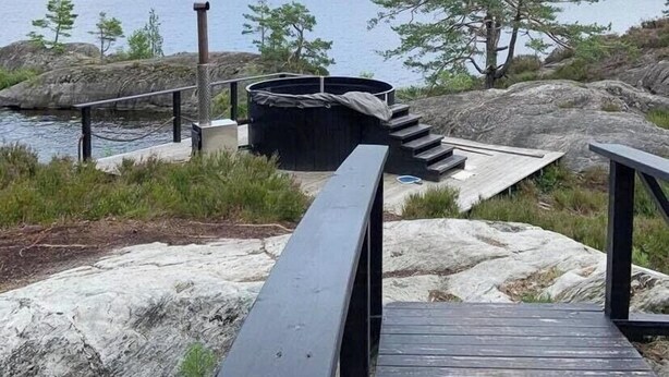 Une terrasse en bois menant à un quai surplombant l’eau, entouré de rochers et d’arbres.