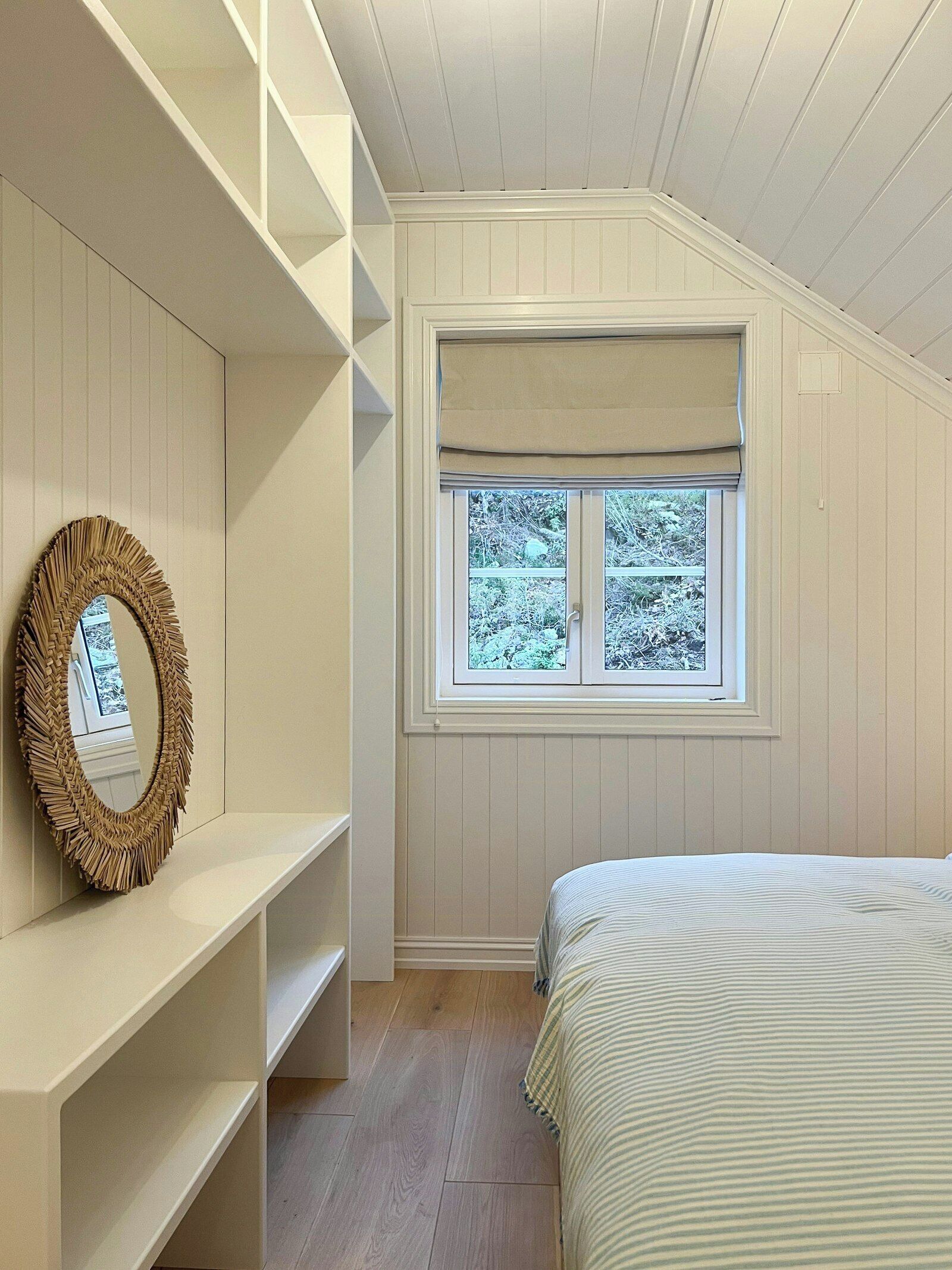 Quarto com cama, janela com vista para árvores, espelho e nichos.