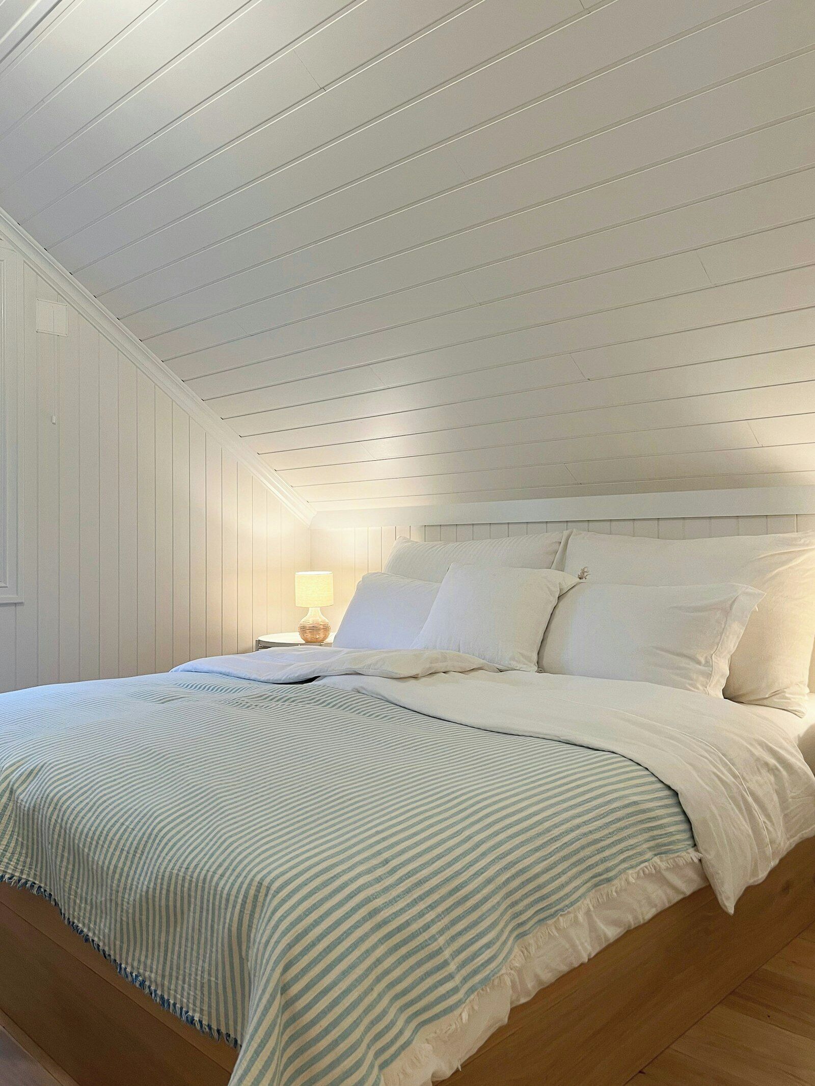 A bedroom with a sloped ceiling, a bed with white bedding, and a nightstand with a lamp.