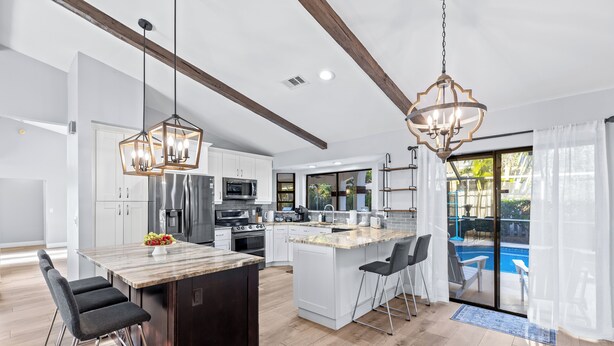 A modern kitchen with a central island, bar stools, and a dining area. - Screened Pool + Firepit + Outdoor Lounge | Mins to WEF + Polo | Palm & Pool (Wellington)