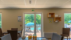 A dining area with wicker chairs, a glass table, breakfast items, and a view of an outdoor pool area. - Cozy Apartment Stay Near Vannes (Plescop)