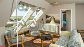 En moderne stue med sofa, lænestole, et sofabord i glas og udsigt gennem ovenlysvinduer.