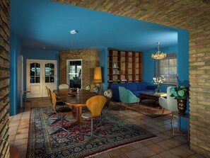 A dining area with a wooden table and chairs, a patterned rug, a bookshelf, and a blue wall.