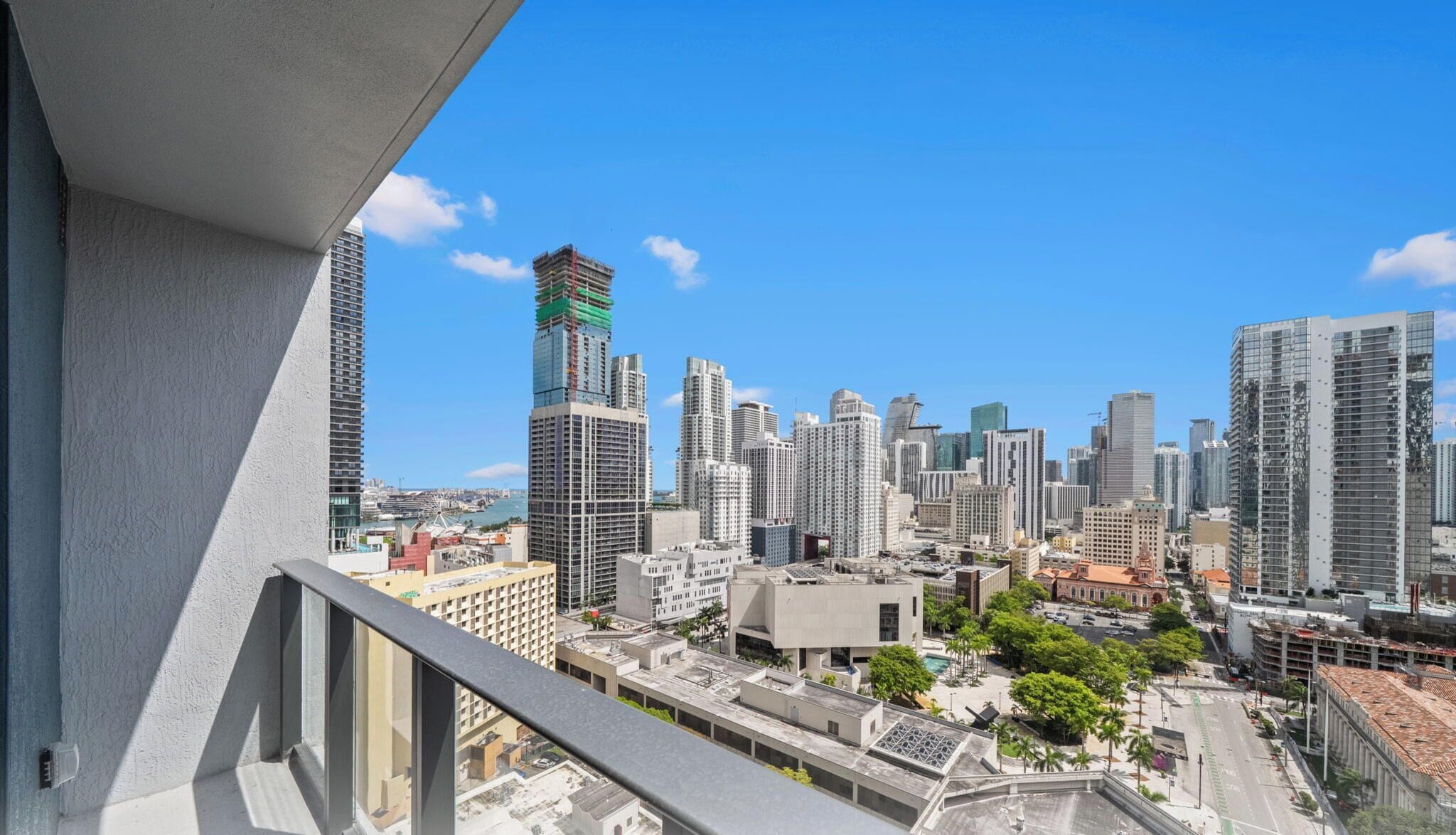 A cityscape with high-rise buildings, a clear sky, and a view from a balcony.