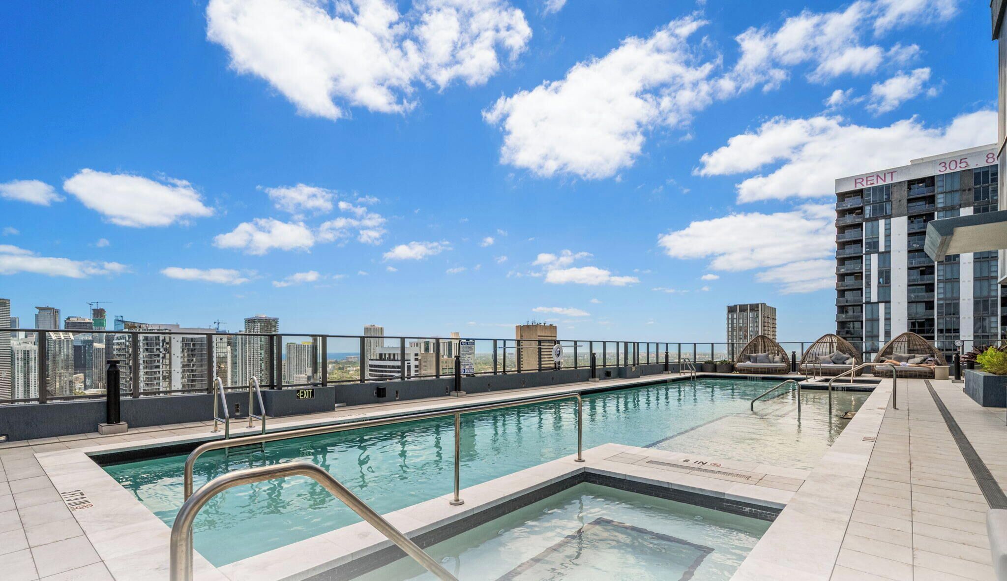 Ein Pool auf dem Dach mit Blick auf die Stadt, ein Schild mit der Aufschrift 'RENT 305' und ein Gebäude mit Balkonen.