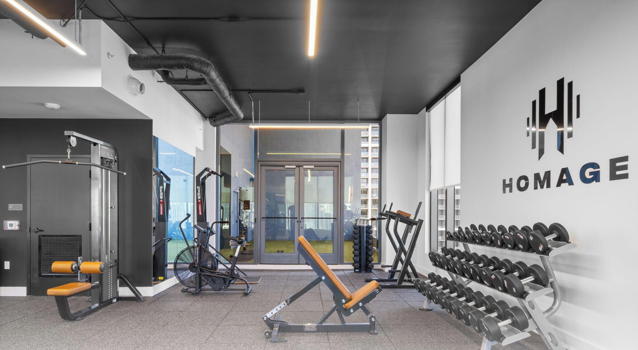 A gym with exercise equipment, a wall-mounted dumbbell rack, and a visible exit door.